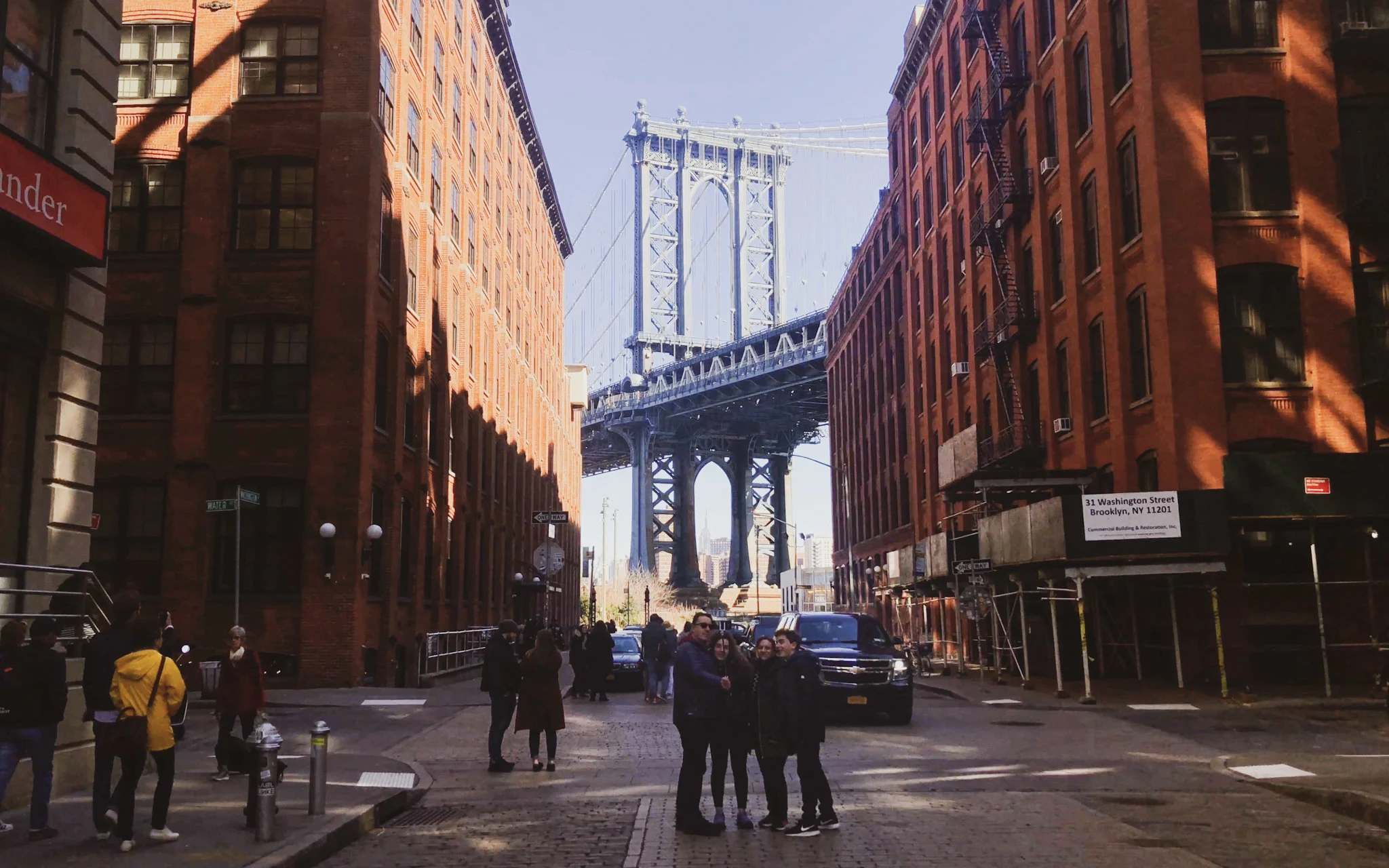 street view in Brooklyn, NY with buildings on each side and the Manhattan Bridge in the distance