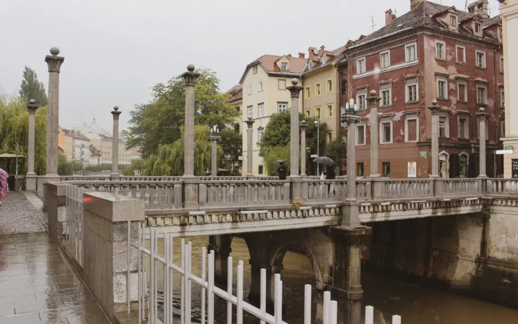 Cobblers Bridge over a river with buildings and trees in Ljubljana, Slovenia