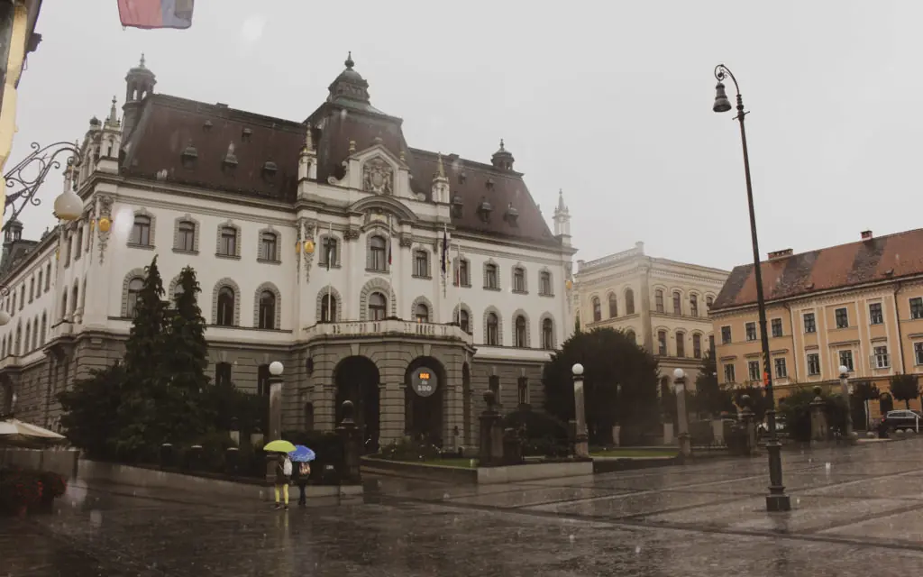 people walking in front of the Museum of Illusions, carrying umbrellas, in Ljubljana, Slovenia