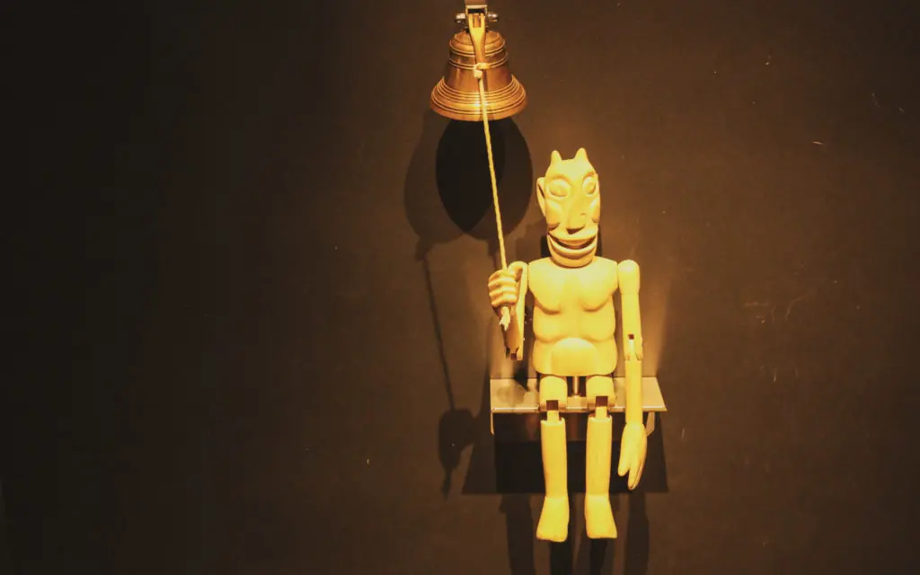 puppet on a shelf holding the rope of a bell