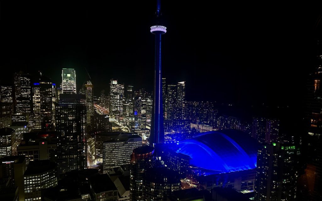 night-time view of the CN tower lit up in blue lights with the city skyline behind it