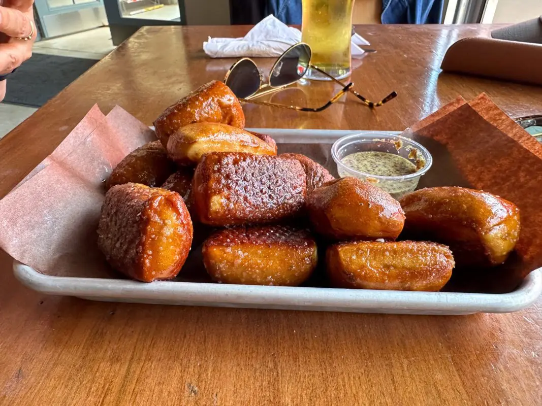 a plate of pretzel bites with a dipping sauce in the center of a wooden table
