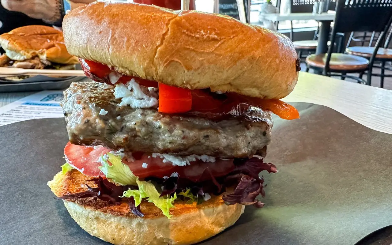 a close-up view of a loaded hamburger with lettuce, tomatoes, and red peppers